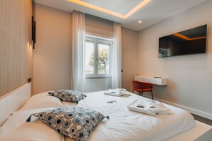 Une chambre d’hôtel avec un lit, un téléviseur fixé au mur, une fenêtre avec des rideaux et un fauteuil rouge.