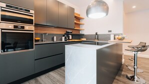 A modern kitchen with built-in appliances, a central island, and bar stools. - Sama Apartments – Elegance, Comfort and Sea View in the Heart of Sorrento (Sorrento)