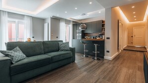 A modern living room with a green sofa, a kitchen area with bar stools, and a dining table. - Sama Apartments – Elegance, Comfort and Sea View in the Heart of Sorrento (Sorrento)
