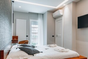 A modern hotel room with a bed, a TV, an air conditioning unit, and a window with a view. - Sama Apartments – Elegance, Comfort and Sea View in the Heart of Sorrento (Sorrento)