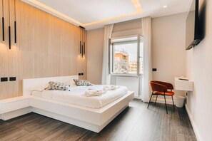 Een moderne slaapkamer met een groot bed, een zithoek, een raam met uitzicht en een wandgemonteerde flatscreen televisie.