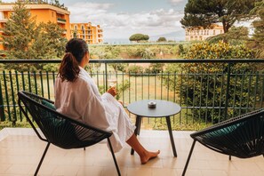 Un balcón con dos sillas y una mesa, con vistas a un jardín y edificios.