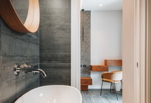 Een moderne badkamer met een vrijstaand bad, een houten wastafelmeubel en een stoel.