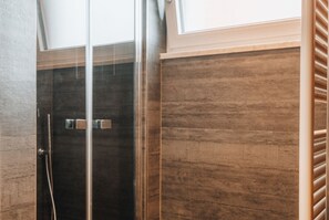 Une douche fermée par des parois en verre, avec un mur en panneaux de bois et une poignée en métal.