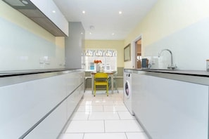 Una cocina moderna y estrecha con armarios blancos, una silla amarilla y una lavadora.