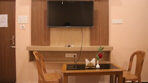 A hotel room with a television mounted on the wall, a wooden table with chairs, and a vase with flowers on the table.