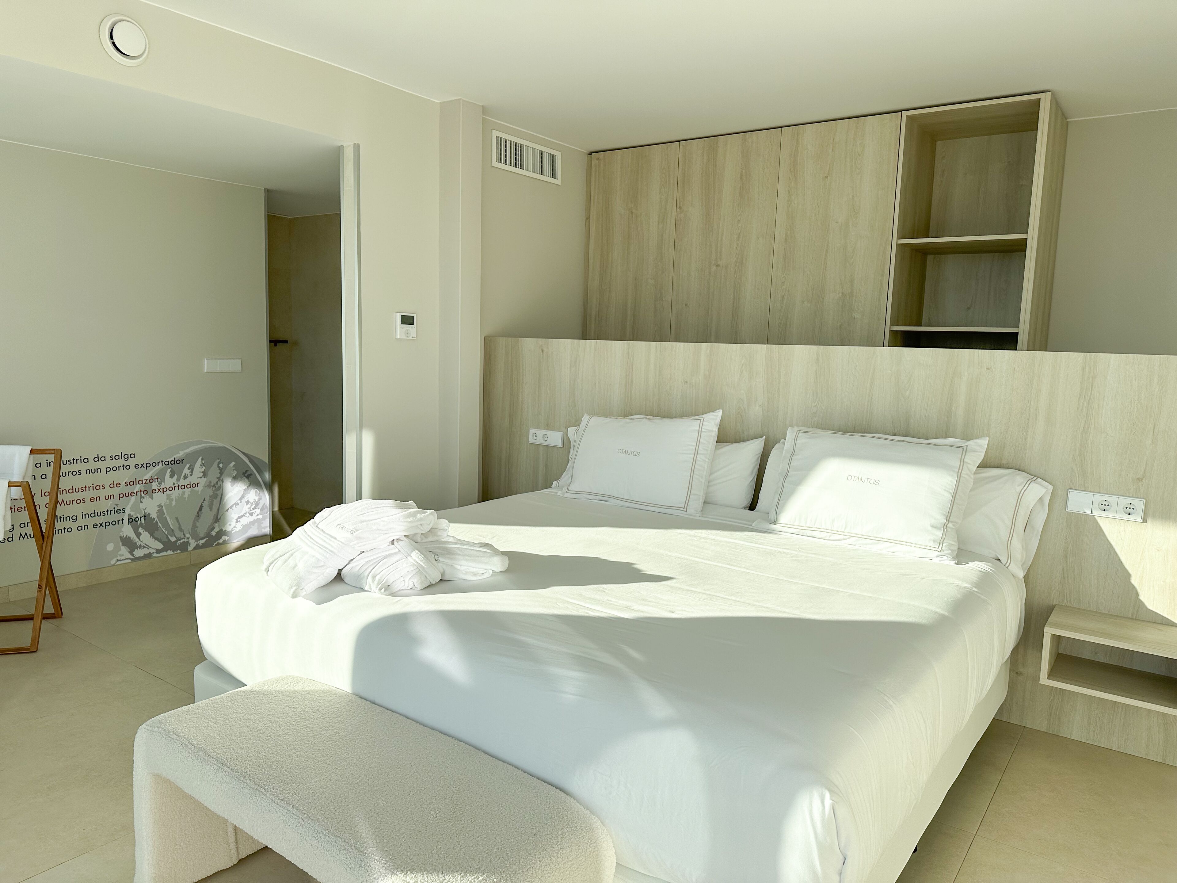 Una habitación de hotel moderna con una cama grande, un cabecero de madera y una estantería empotrada sobre la cama.