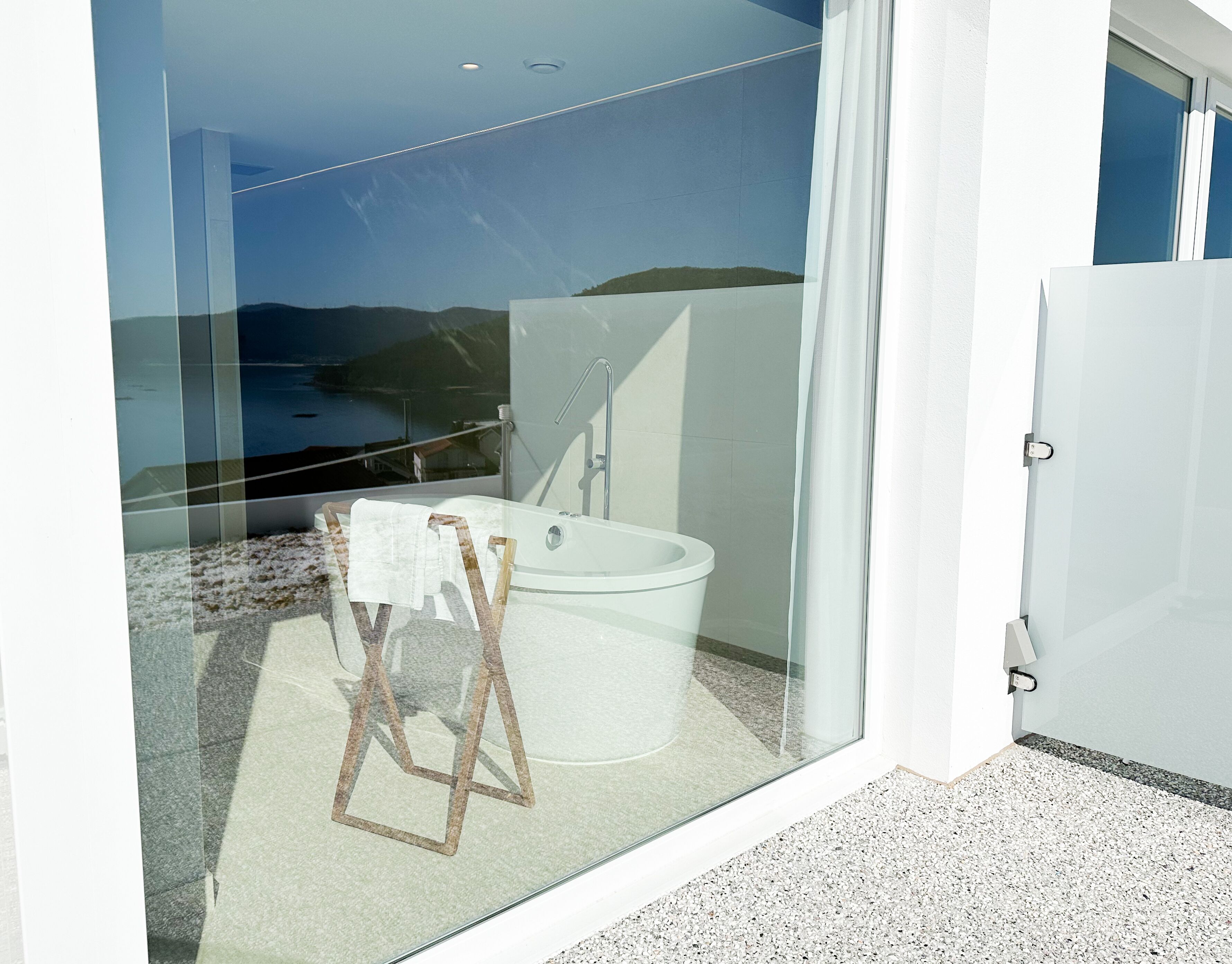 Un baño moderno con bañera, ducha y un balcón con cerramiento de vidrio que ofrece vistas panorámicas.