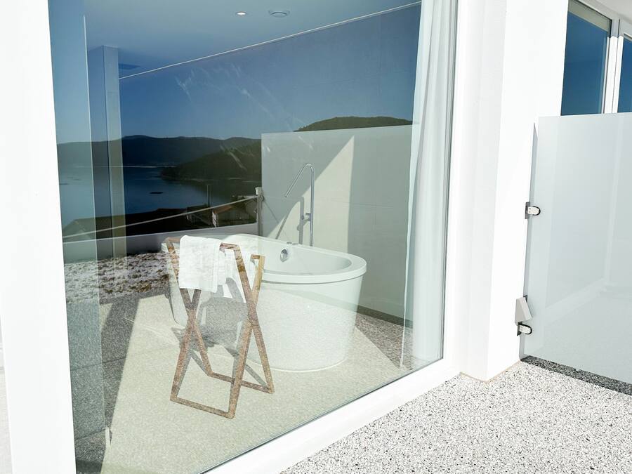 Un baño moderno con bañera, ducha y un balcón con cerramiento de vidrio que ofrece vistas panorámicas.