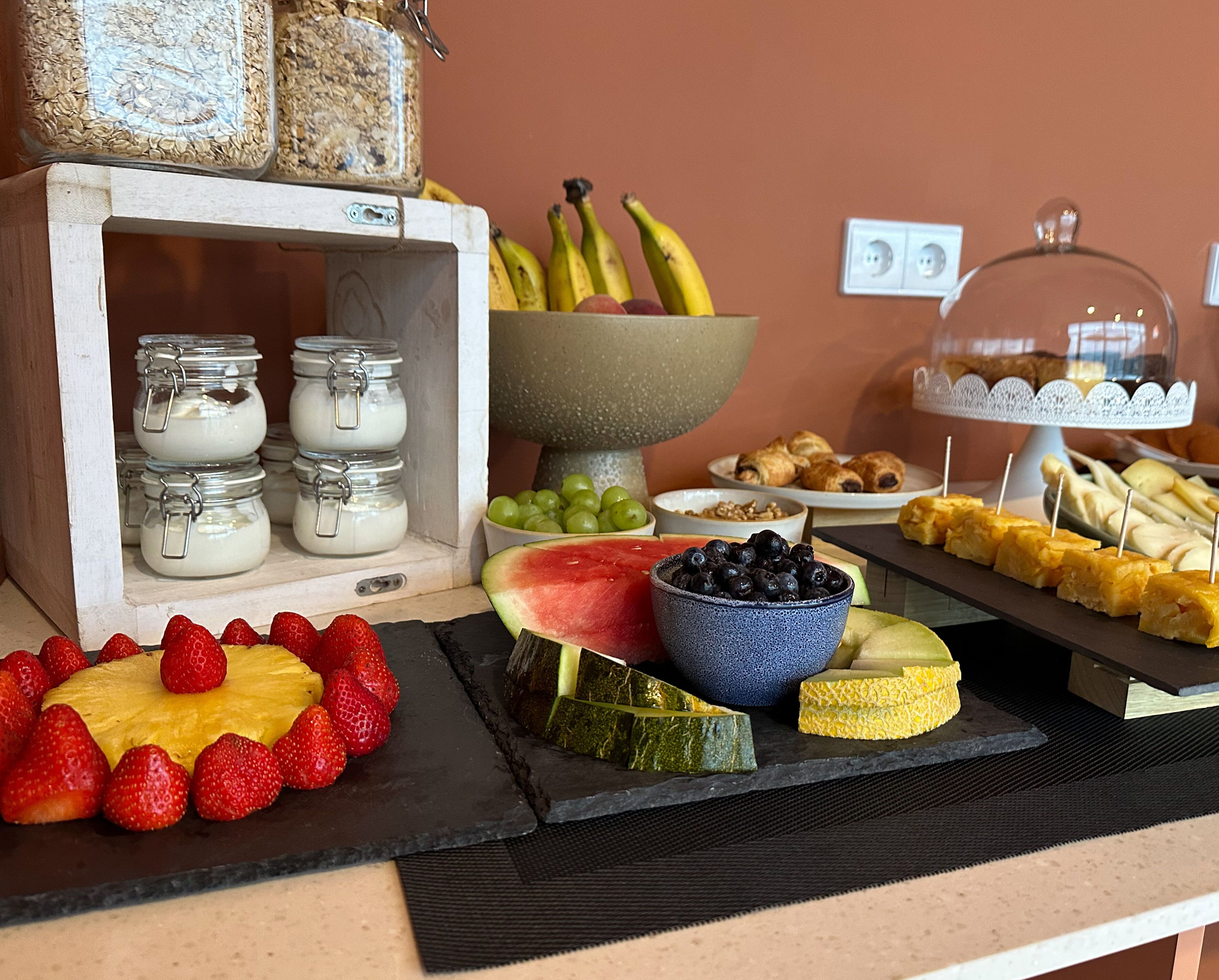 A buffet with various food items including fruits, pastries, and a bowl of grapes.