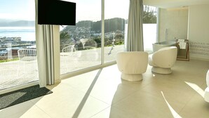 A modern hotel room with a large window offering a scenic view of a coastal town and the sea. - Otantus Hotel (Muros)