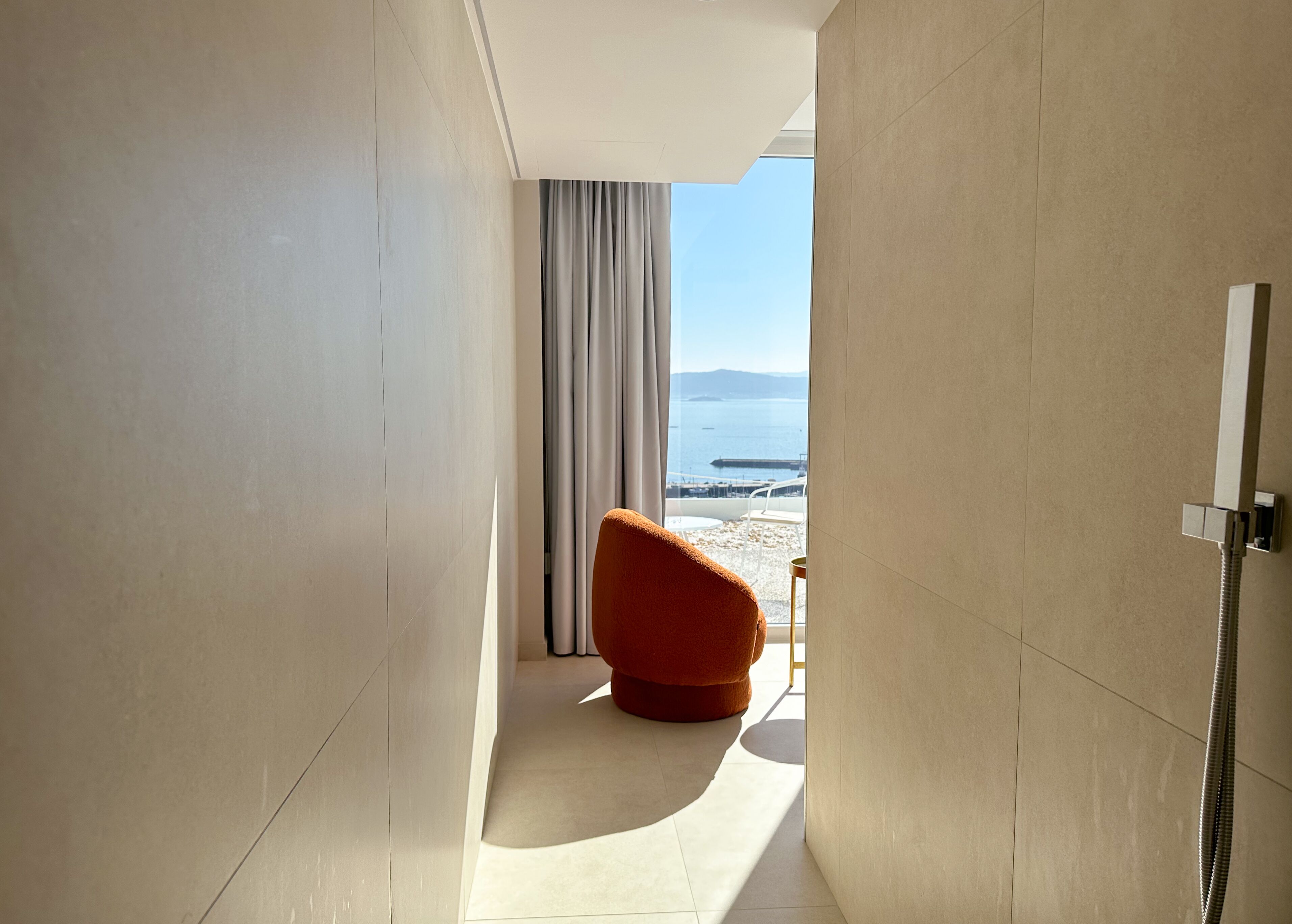 A modern bathroom with a shower, a view of the beach, and a red chair.