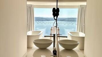 Un baño moderno con dos lavamanos blancos amplios, un espejo y vista al mar.