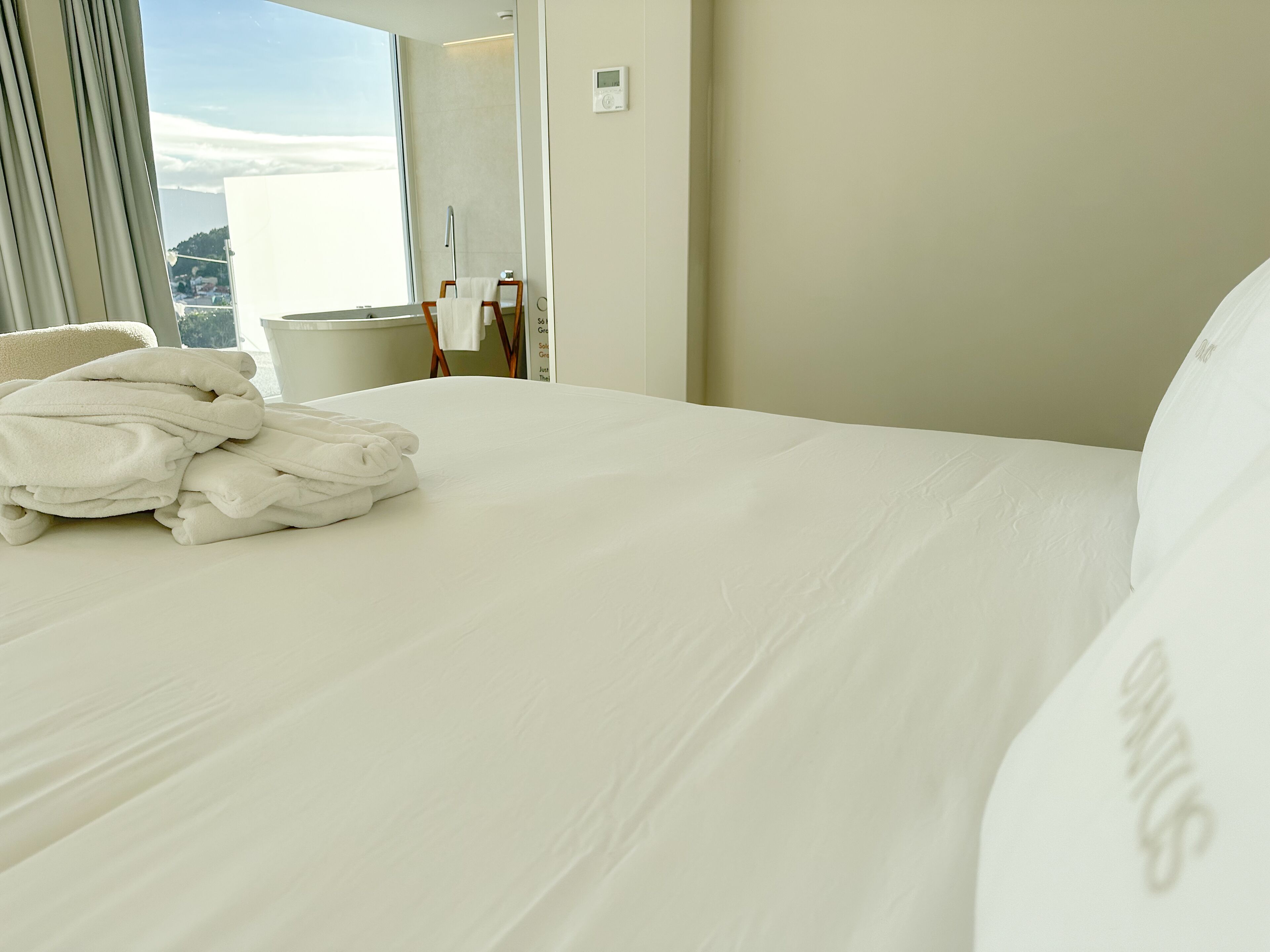 Habitación de hotel con una cama bien hecha, una ventana con cortinas y vistas al exterior.