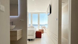 A modern bathroom with a large window, a sink, and a bed with a view of the sea. - Otantus Hotel (Muros)