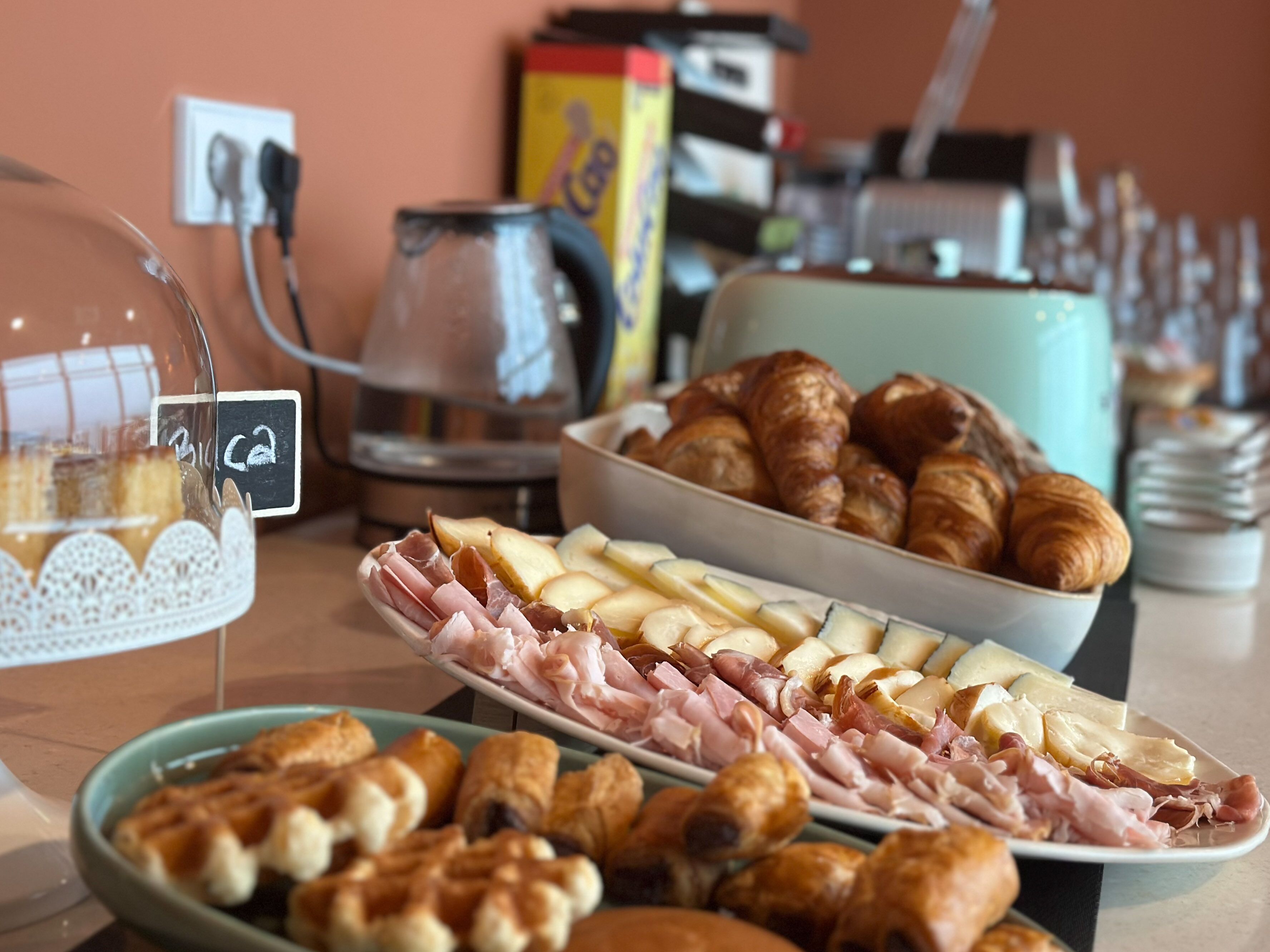 A breakfast buffet with various food items including pastries, meats, and cheeses.