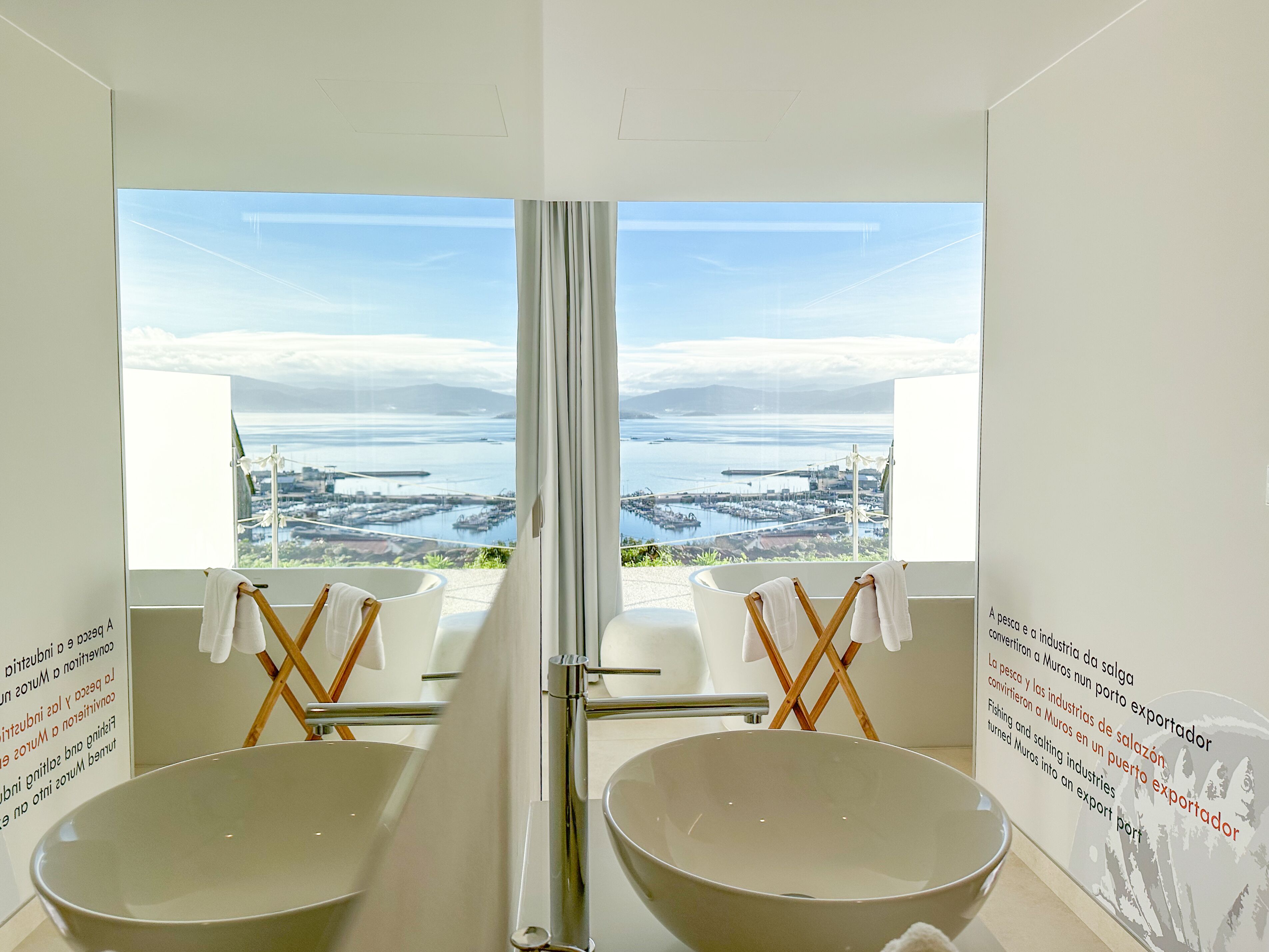 Un baño con dos lavamanos grandes, vistas a una ciudad costera y un espejo que refleja la panorámica.