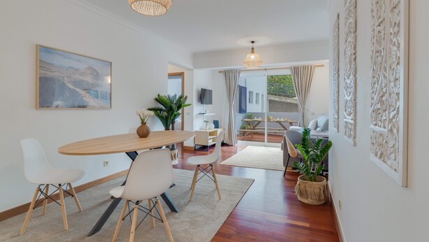 Un espace repas moderne avec une table en bois, des chaises blanches et des lampes en osier suspendues au plafond.
