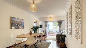 Un espace repas moderne avec une table en bois et des chaises blanches, un luminaire suspendu et un tableau au mur.