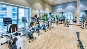 Un gimnasio moderno con diversas máquinas de cardio, estaciones de pesas y un amplio espejo a lo largo de la pared.