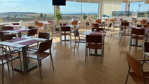 A spacious dining area with tables and chairs, large windows offering a view of the countryside, and a mounted television. - Motel 112 Algora  (Algora)
