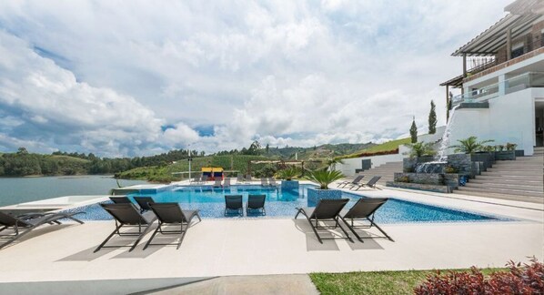 Relax by the pool surrounded by lush greenery and a serene lake view.