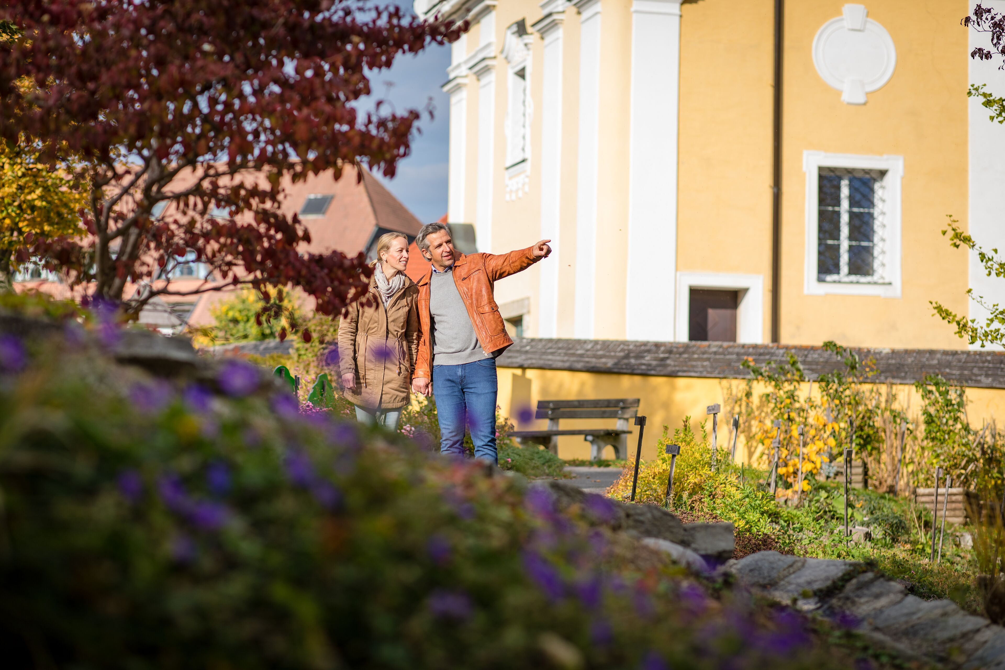 A couple standing in a garden with a yellow building in the background.