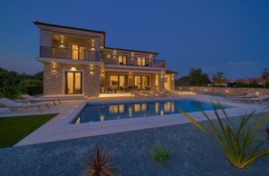 Uma casa moderna de dois andares com piscina, área de estar externa e uma varanda bem iluminada.