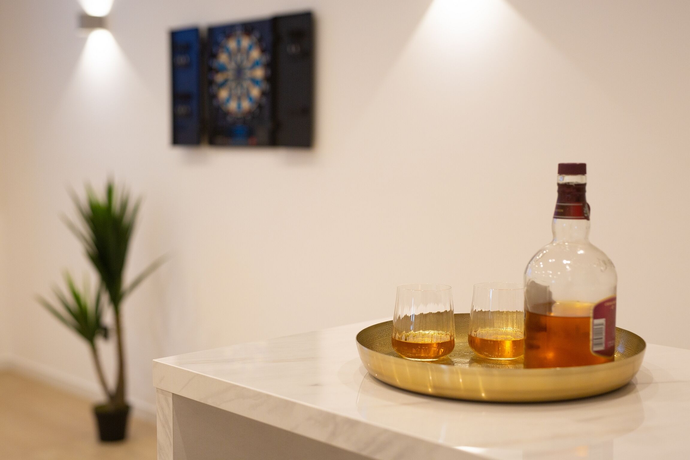 A bar area with a bottle of liquor, two glasses, and a tray on a marble countertop.