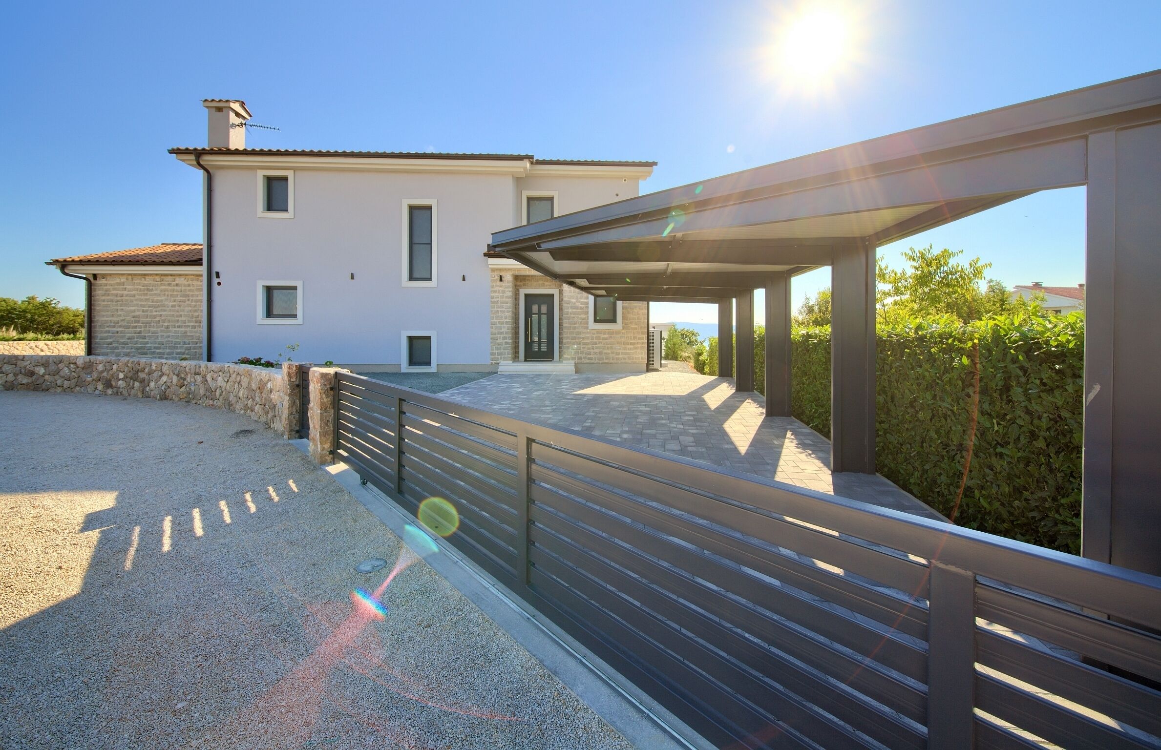 A modern house with a paved driveway, a covered outdoor area, and a stone wall.