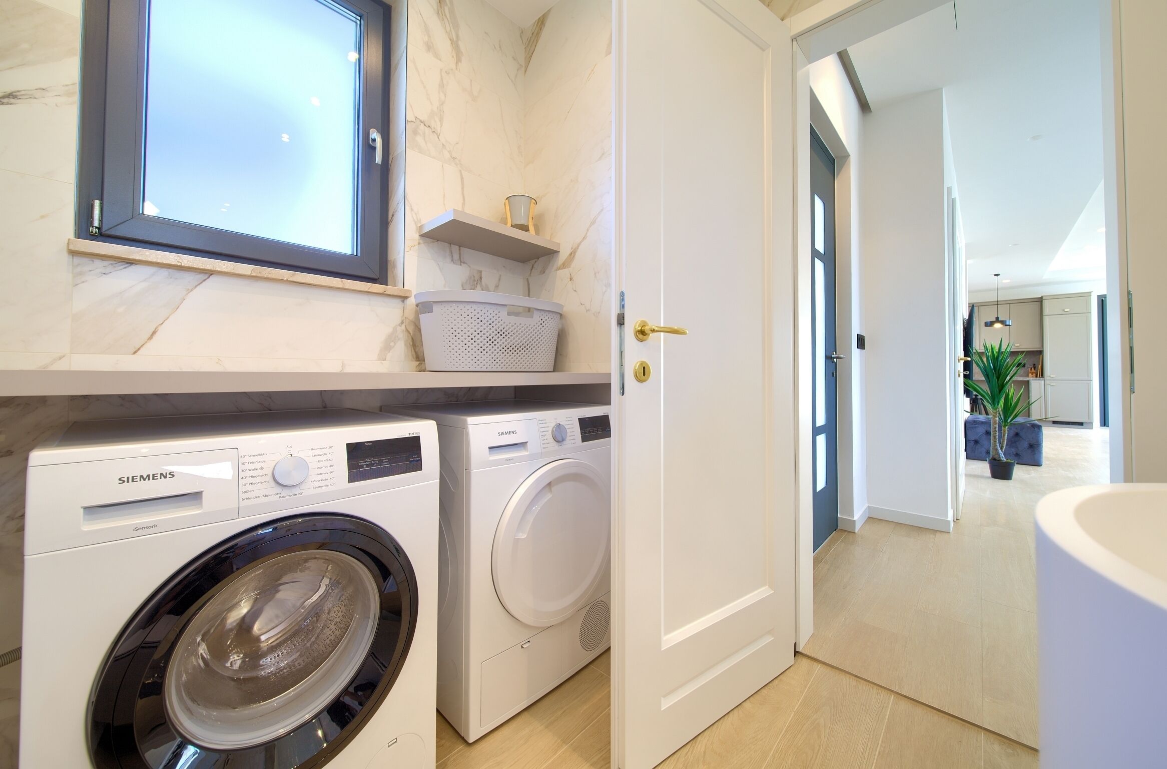 Une buanderie moderne équipée d’un lave-linge Siemens, d’une grande fenêtre et d’une porte donnant sur une salle de bain.