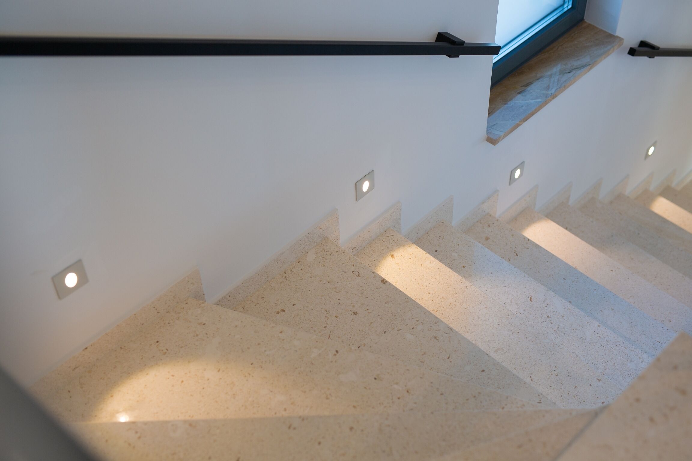 Un escalier muni d’une rampe, d’appliques et d’une fenêtre.
