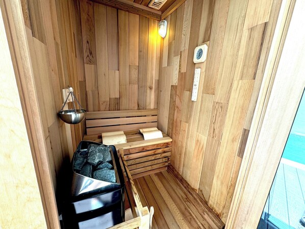 A sauna with wooden walls, a bench, a metal basin, and a heater.