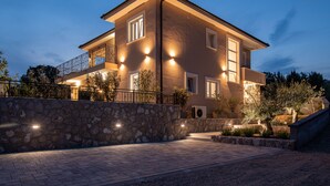 Una casa a due piani con un muro in pietra, diverse finestre e illuminazione esterna.