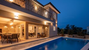 Una casa moderna a due piani con piscina, zona pranzo all'aperto e un balcone con ringhiera decorativa.