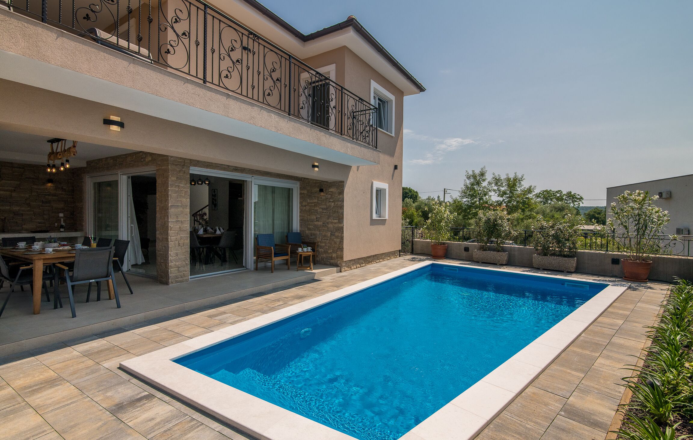 A two-story house with a swimming pool, outdoor seating, and a balcony with decorative railing.