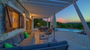 An outdoor patio with a stone floor, a sofa, a table, and a pool in the background. - Villa Laura with pool and jacuzzi (Kvarner - Brusići) (Brusići)