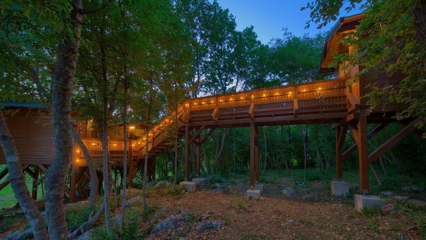 A wooden treehouse with a wooden deck and string lights, surrounded by trees and rocks. - Villa Laura with pool and jacuzzi (Kvarner - Brusići) (Brusići)