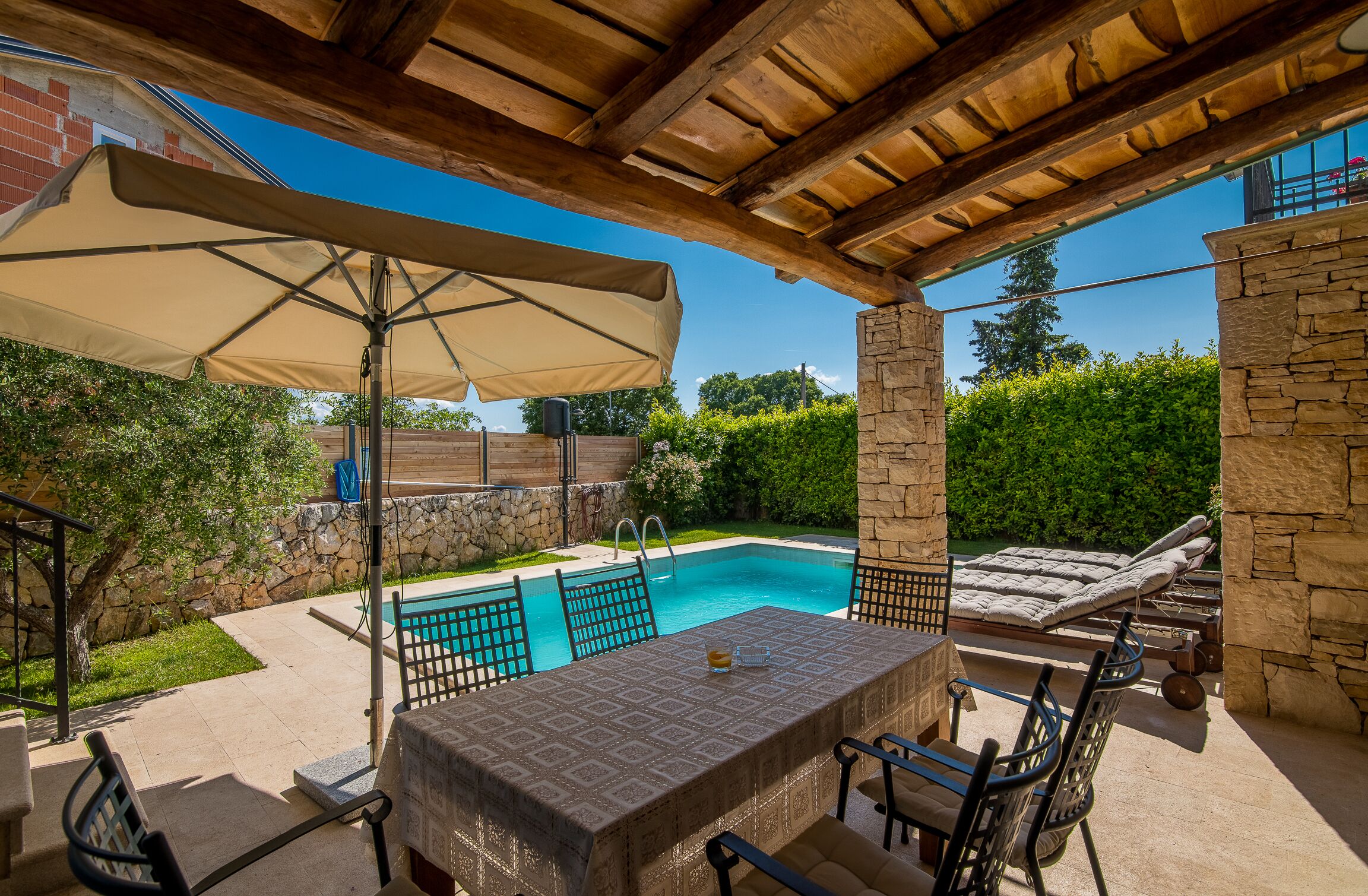 An outdoor patio with a pool, stone walls, and a covered seating area.