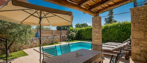 An outdoor patio with a pool, stone walls, and a covered seating area.