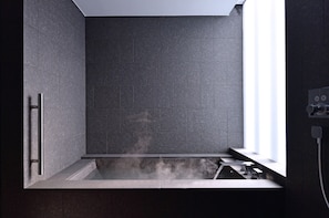 Une salle de bain moderne dotée d’une baignoire intégrée, d’un espace douche et d’une fenêtre laissant entrer la lumière naturelle.