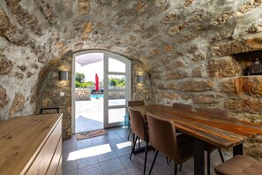 Enjoy meals in this stylish dining area with a large table and comfortable chairs, leading to an outdoor space with a pool.