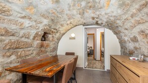 Una habitación rústica con paredes de piedra, una mesa y sillas de madera, un aparador de madera y una pequeña lámpara circular en la pared.