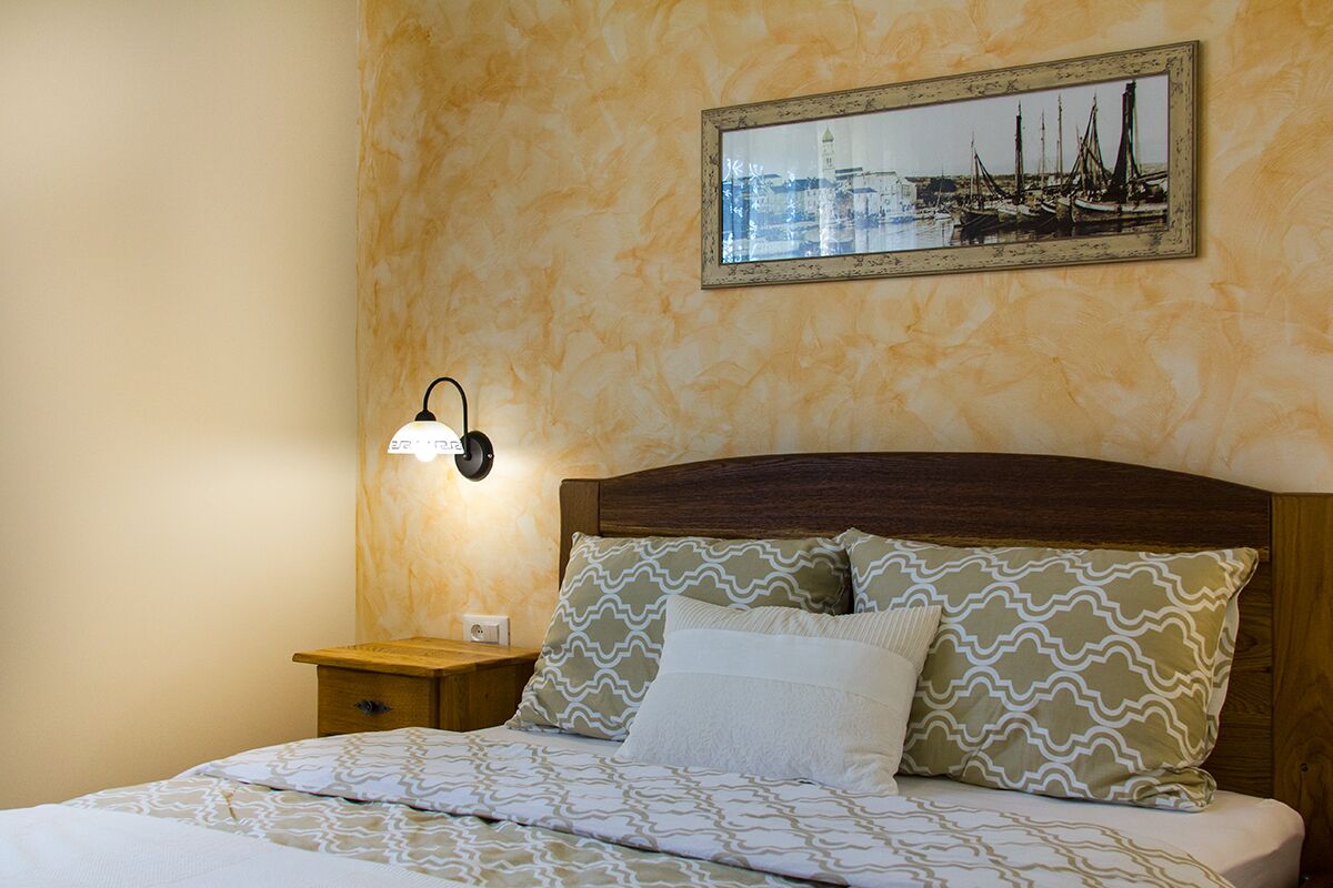 A hotel room with a bed, a nightstand, a wall-mounted lamp, and a framed picture of a harbor.