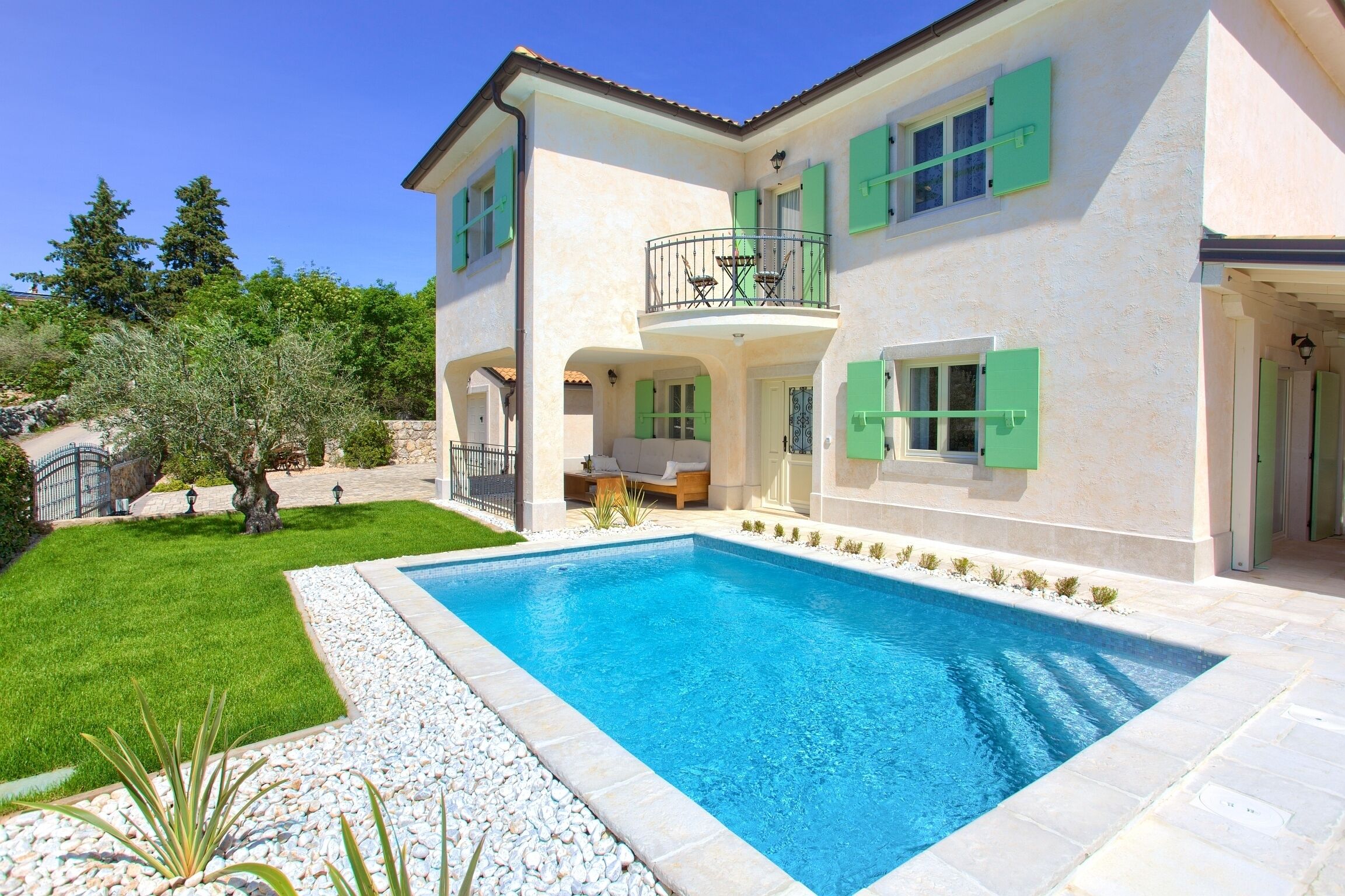 Une maison à deux étages avec une piscine, des volets verts et un balcon.