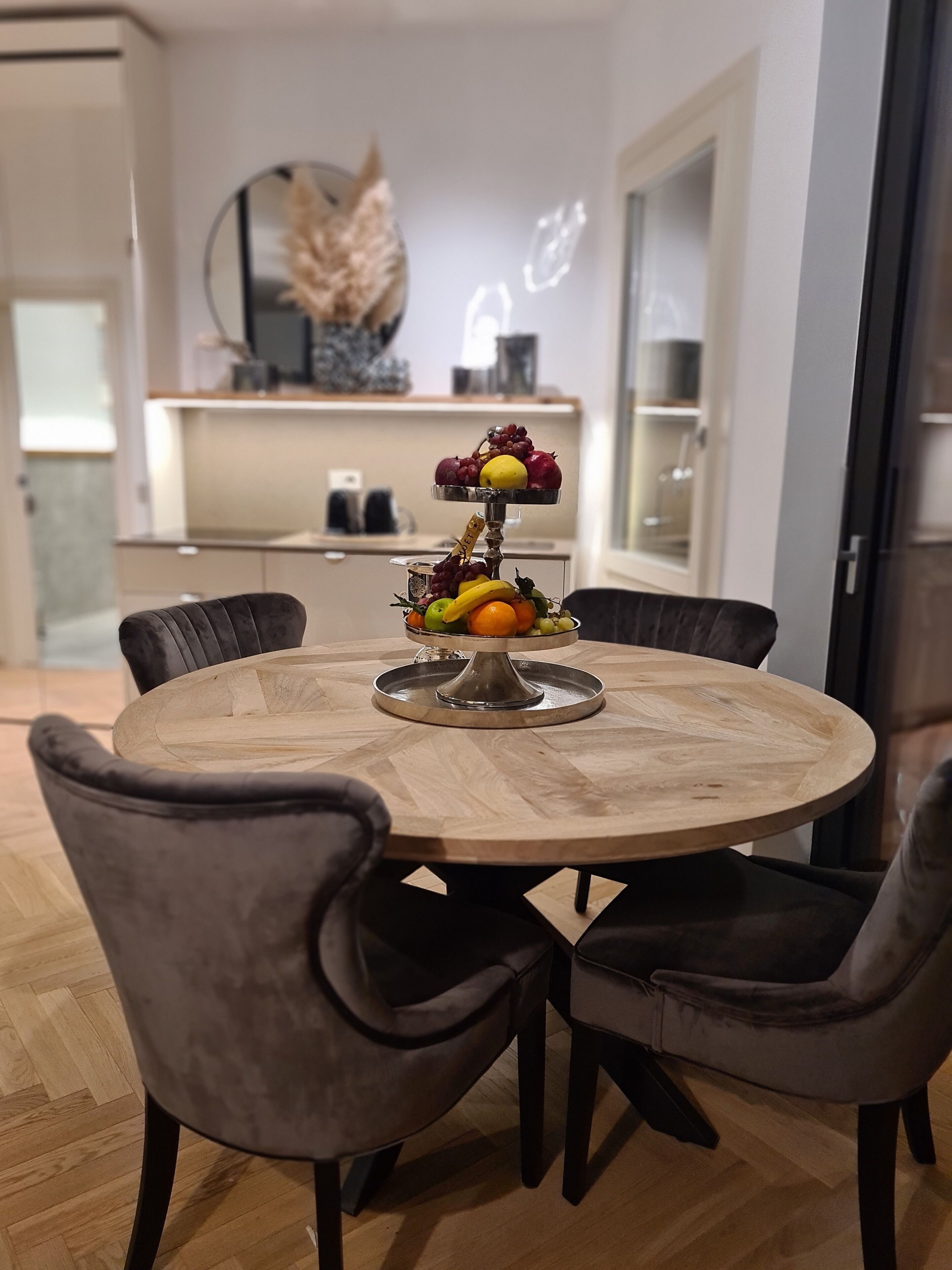 A round dining table with a fruit centerpiece, surrounded by four upholstered chairs.