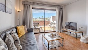 Un salon moderne comprenant un canapé, une table basse, un téléviseur et un balcon aménagé avec du mobilier d’extérieur.