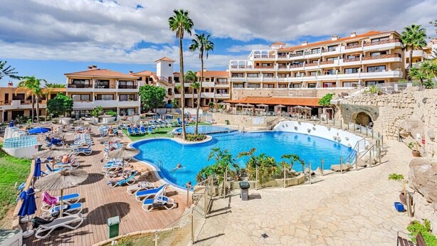 Un hôtel doté d’une piscine, de chaises longues et de palmiers.