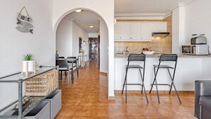 Une cuisine moderne avec des meubles blancs, un îlot central doté de tabourets de bar et un coin repas avec une table et des chaises en verre.
