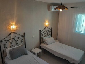 Ein Schlafzimmer mit zwei Betten, jeweils mit Kopfteil und Nachttischen. An beiden Seiten der Betten befinden sich Wandlampen.